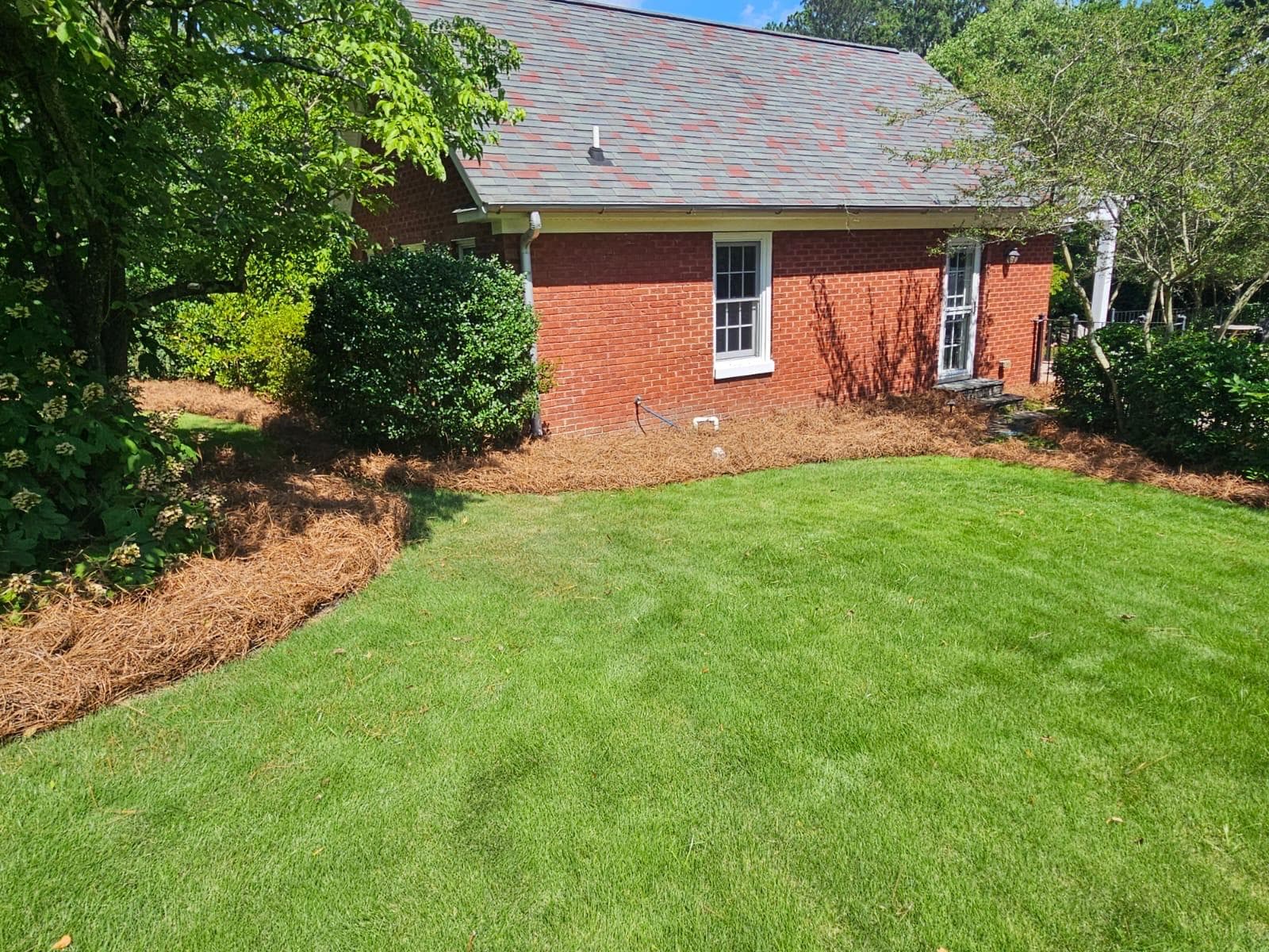 Red brick house with a shingle roof, pine straw mulch, and a lush green lawn.