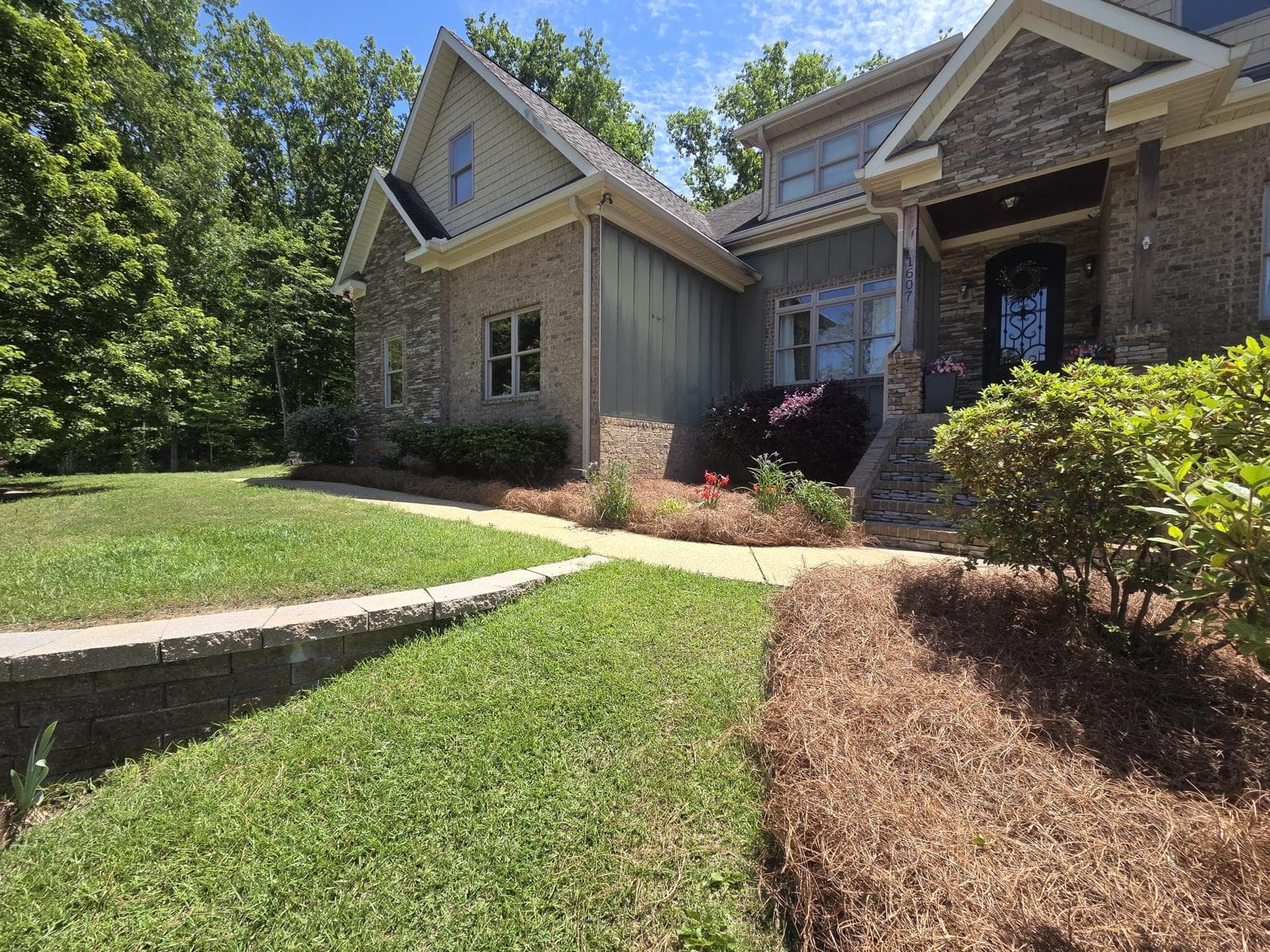 Large brick and stone house with gabled roofs, green lawn, and pine straw landscaping.